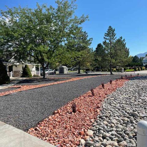 Landscaped yard with gravel paths, red rock border, trees, and a clear blue sky