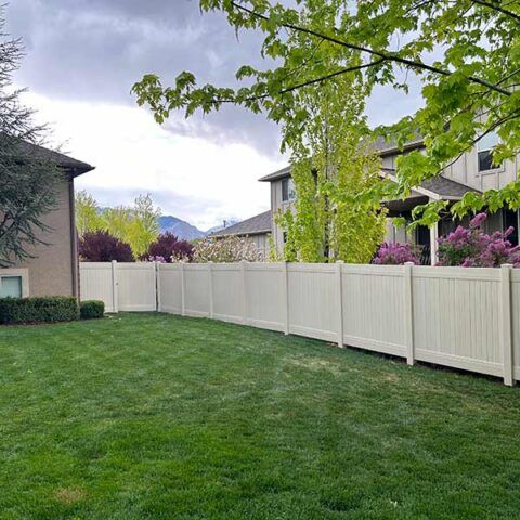 Suburban backyard with green lawn, white fence, and leafy tree branches framing a mountain view