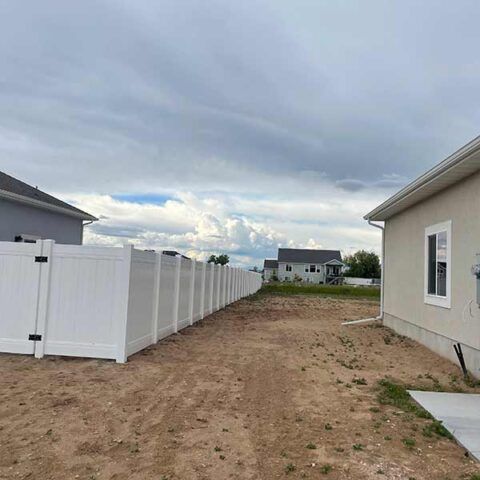 Backyard with dirt path between a white fence and a beige house under a cloudy sky