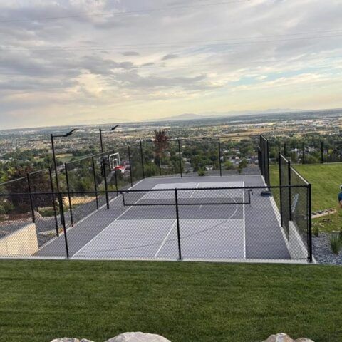 Outdoor pickleball court with black fencing and a scenic city and mountain view beyond.