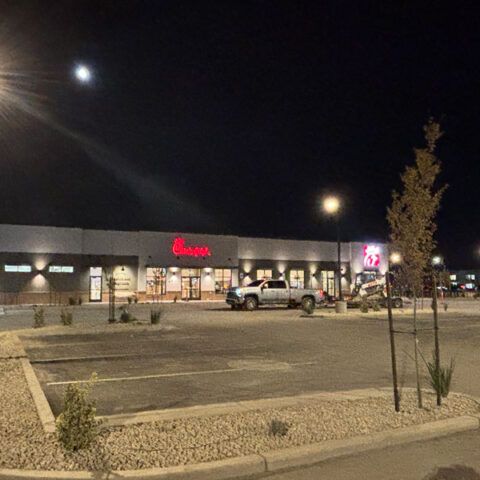 Nighttime view of a strip mall parking lot with a parked white pickup truck and lit storefronts