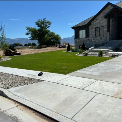 Stone house with a neatly landscaped green lawn, concrete driveway, and desert mountain backdrop