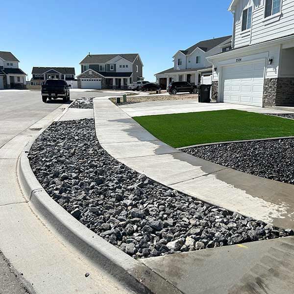 Curved concrete and rock landscaping beside a suburban street with houses and a parked truck