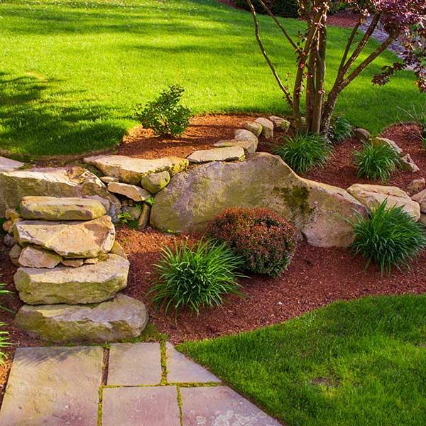 Stone steps beside a landscaped garden bed with rocks, shrubs, and green lawn.