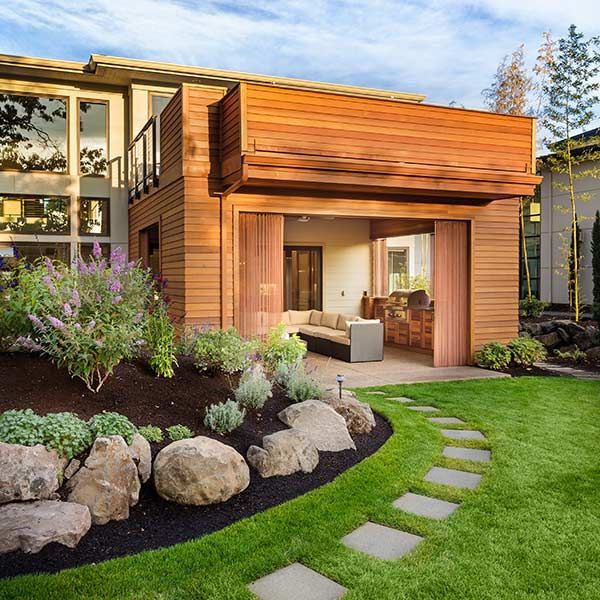 Modern house with wood exterior, landscaped garden, and stone path leading to a covered patio