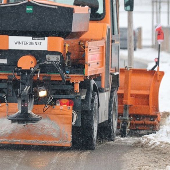Orange snowplow clearing slushy street in falling snow