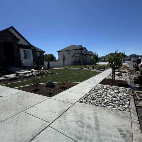 New suburban front yard with concrete walkways, fresh landscaping, and rock beds under a clear blue sky