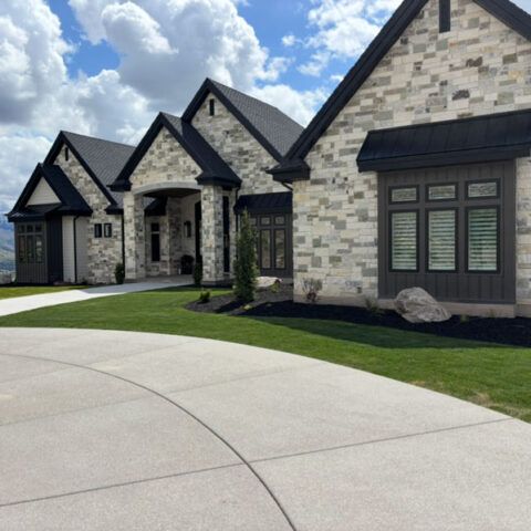 Modern stone houses with dark roofs along a curved driveway under a bright blue sky