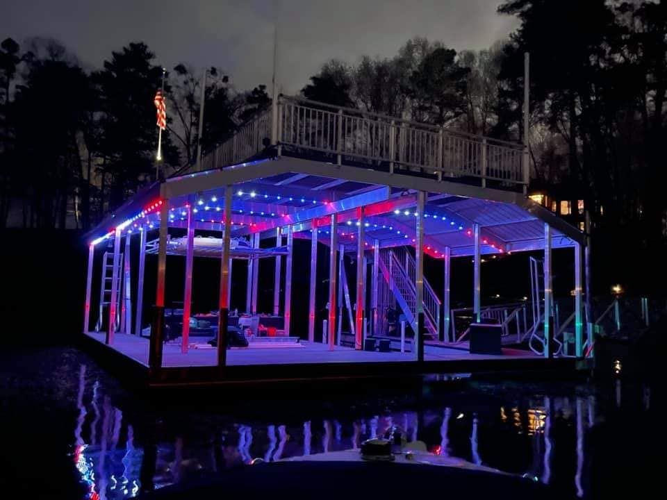 A dock with christmas lights on it is lit up at night.