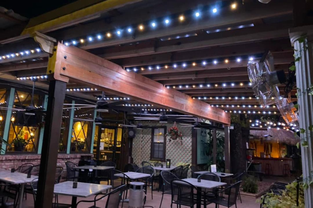 A restaurant with tables and chairs under a pergola at night.