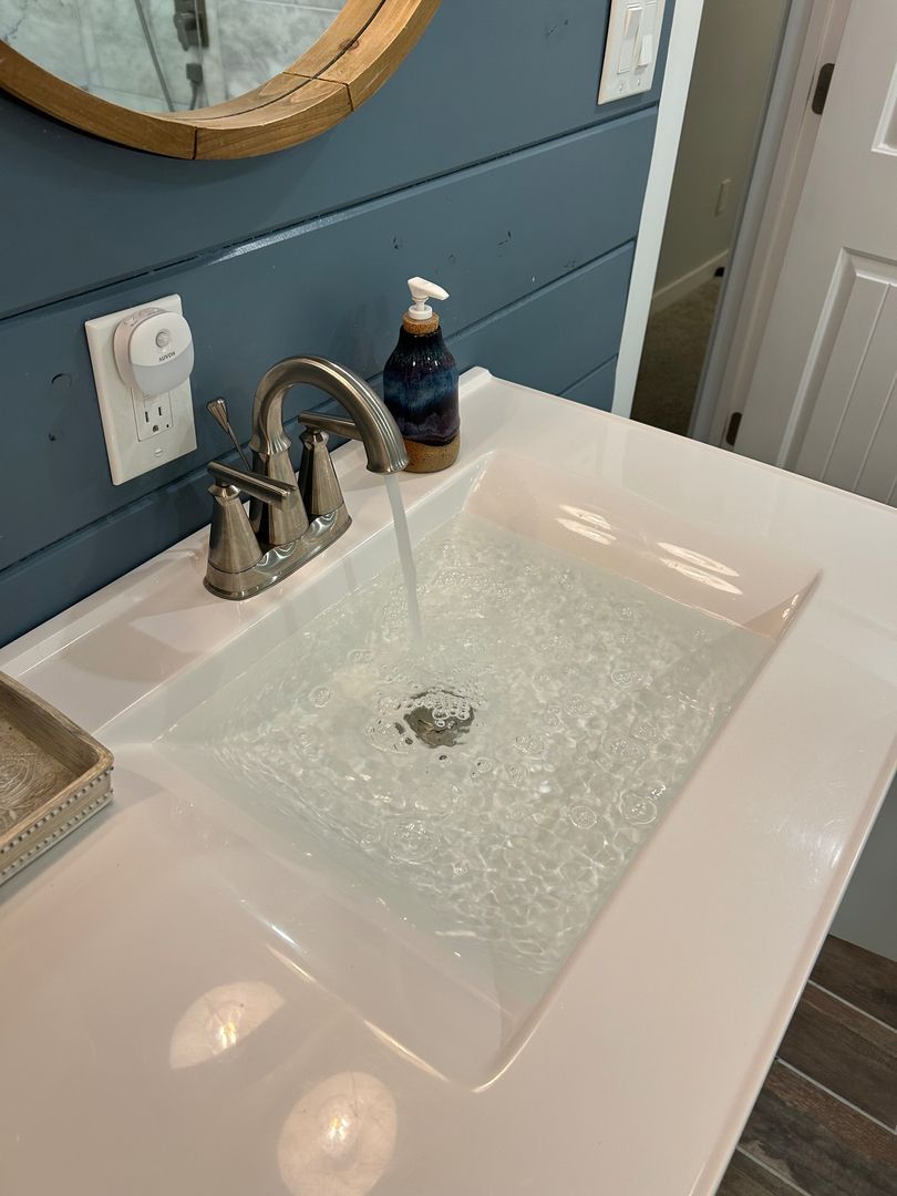 Bathroom sink with water running into a white countertop basin, blue wall, and mirror above
