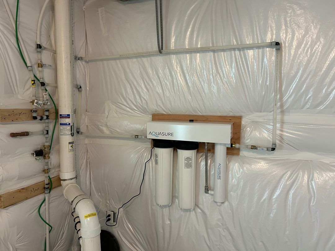 Wall-mounted water filter system with pipes and white insulation in a utility room