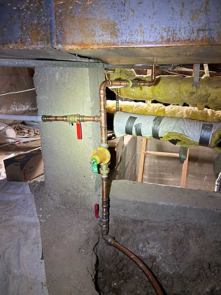 Rusty underground pipework with valves and a yellow pressure gauge in a concrete utility space