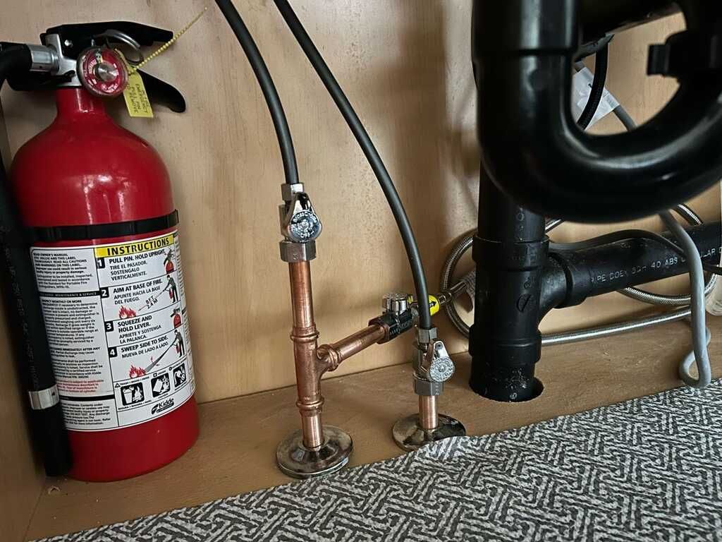 Fire extinguisher beside copper pipes and black plumbing in a carpeted utility area.