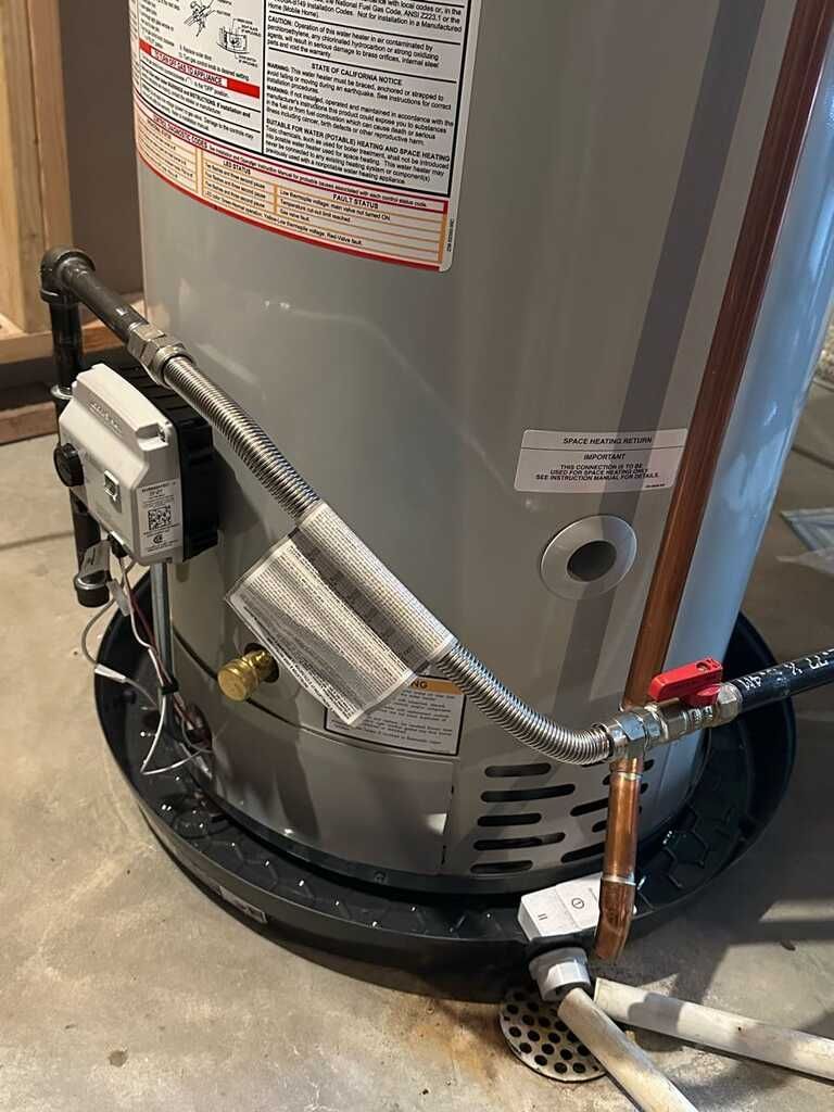 Water heater with attached pipes, valves, and wiring in a utility area.