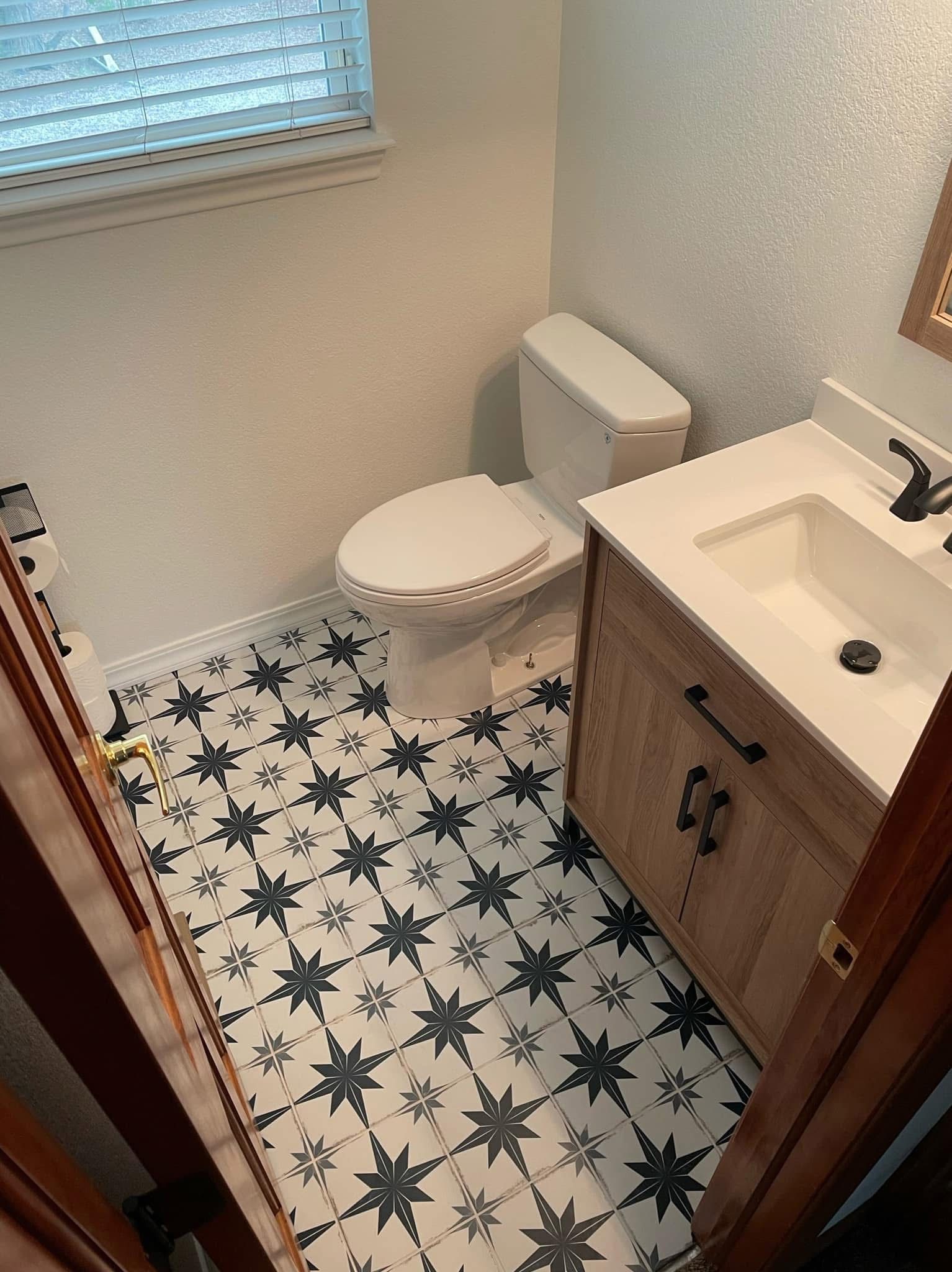 Small bathroom with patterned tile floor, white toilet, and wood vanity with sink.
