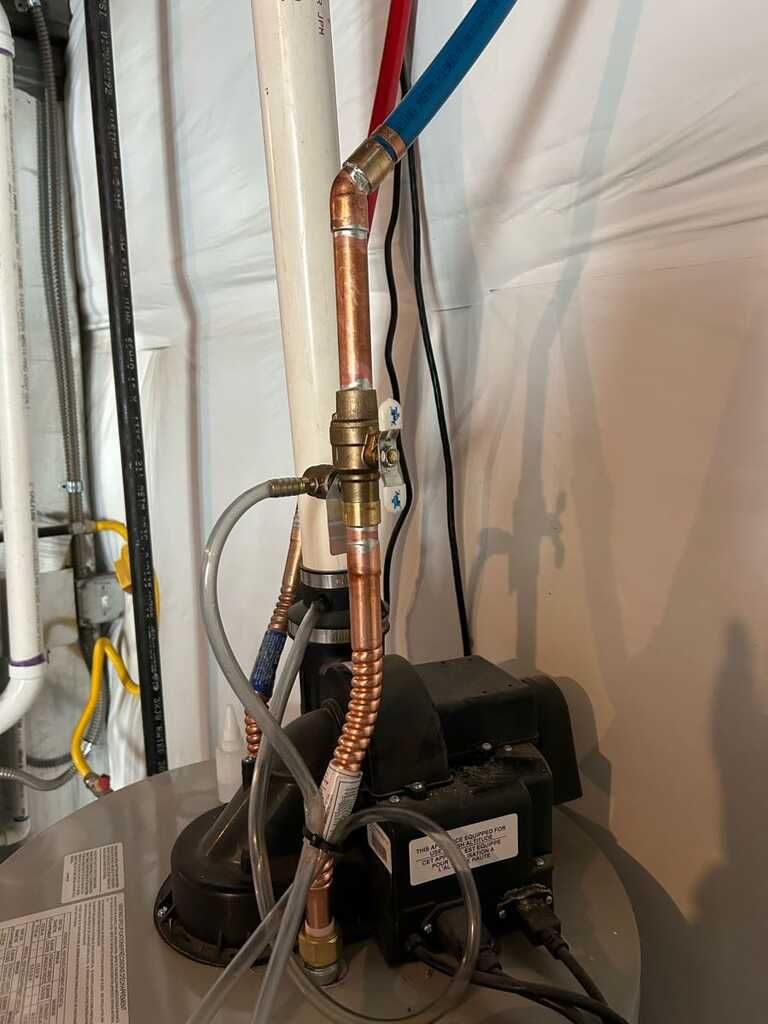 Black HVAC compressor with copper piping and blue insulation in a utility room