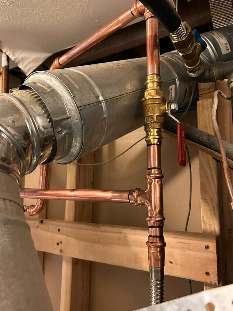 Copper plumbing pipes and ductwork inside an unfinished wall framing, with a red-handled valve.