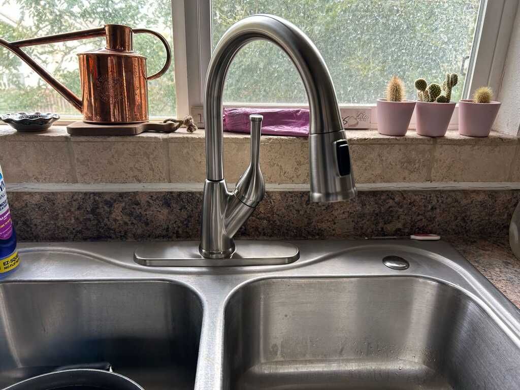 Kitchen sink beneath a window with a chrome faucet, copper kettle, and small potted plants on the sill