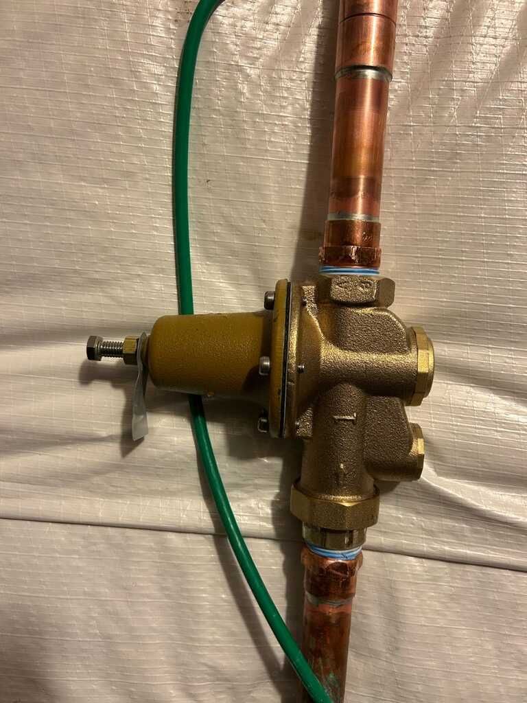 Brass plumbing valve connected to copper pipes and a green hose on a white surface