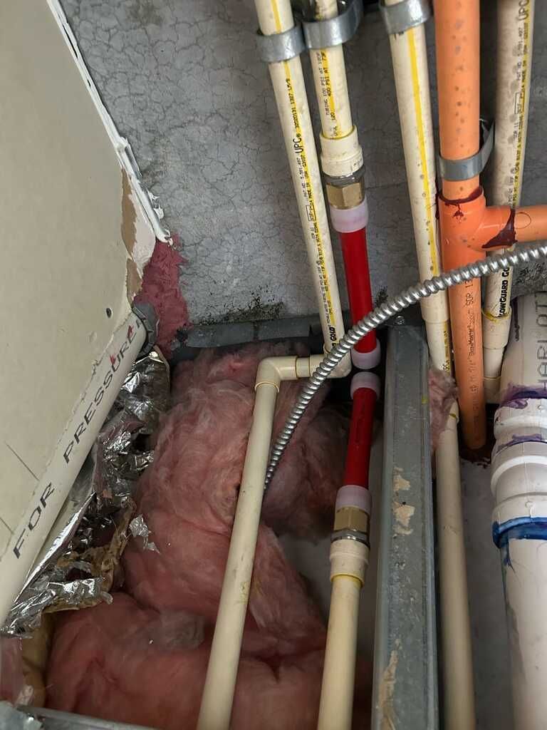 Exposed plumbing pipes beside pink insulation inside an unfinished wall cavity