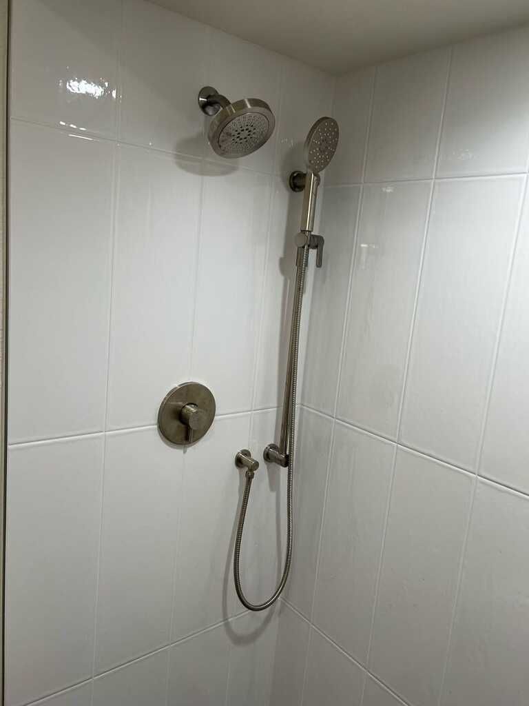 White tiled shower with chrome showerhead, handheld sprayer, and controls.