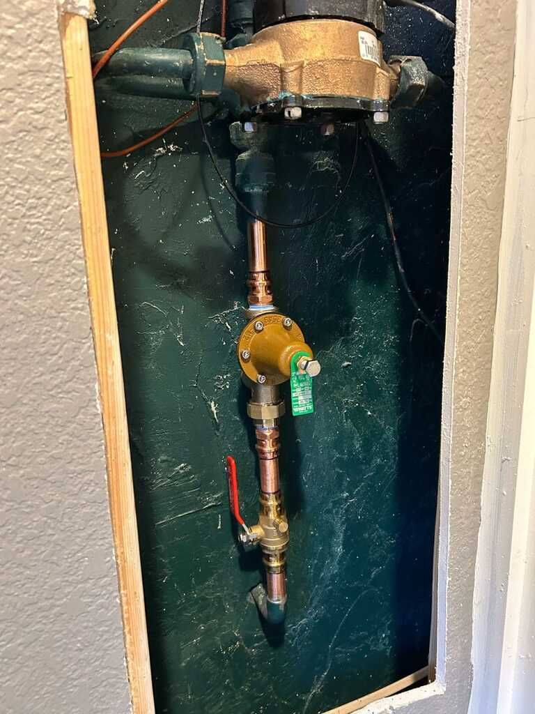 Copper plumbing valve and pipe inside a wall cavity with green insulation.