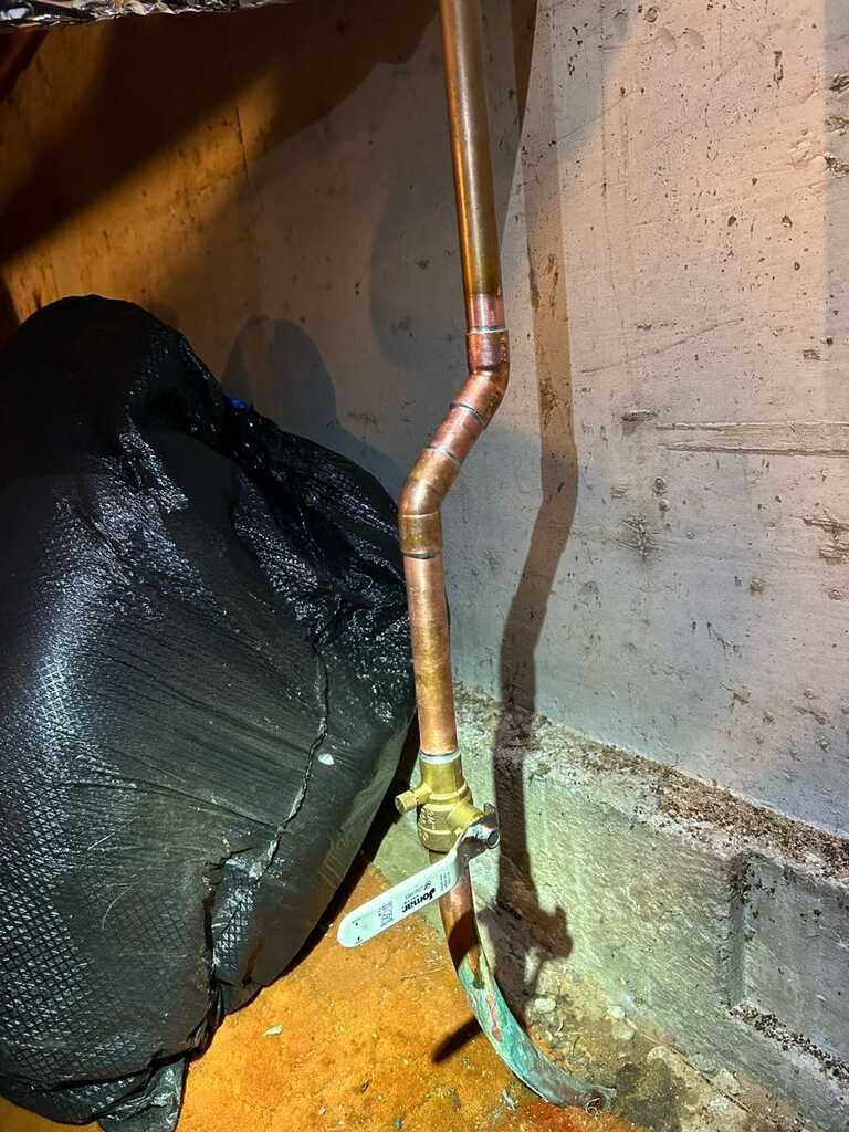 Copper pipe with a valve beside a concrete wall and black tarp in a basement corner