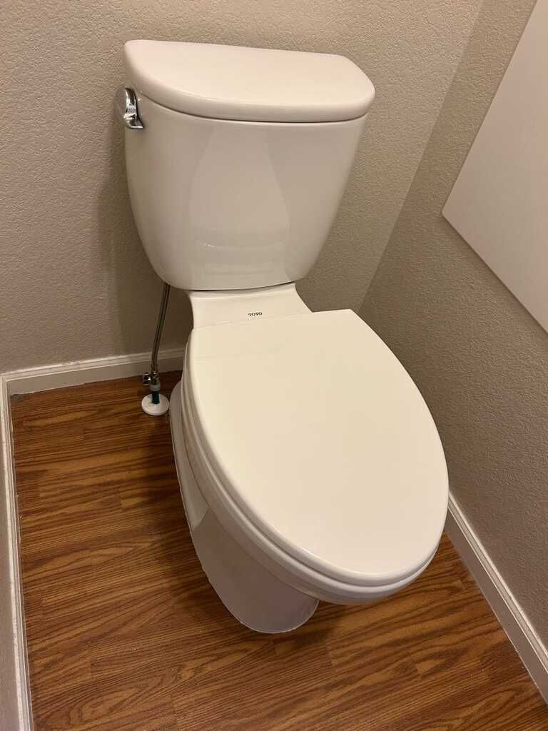 White toilet in a small bathroom with wood-look flooring and beige walls.