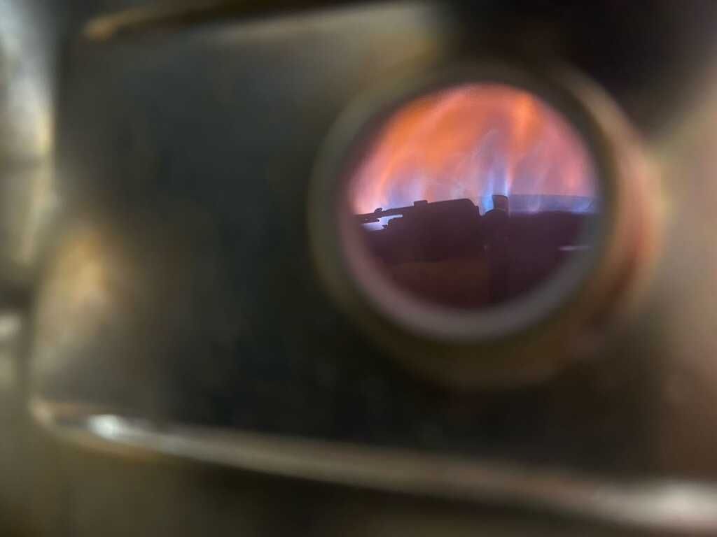 Circular window showing a purple-blue flame inside a dark metal chamber