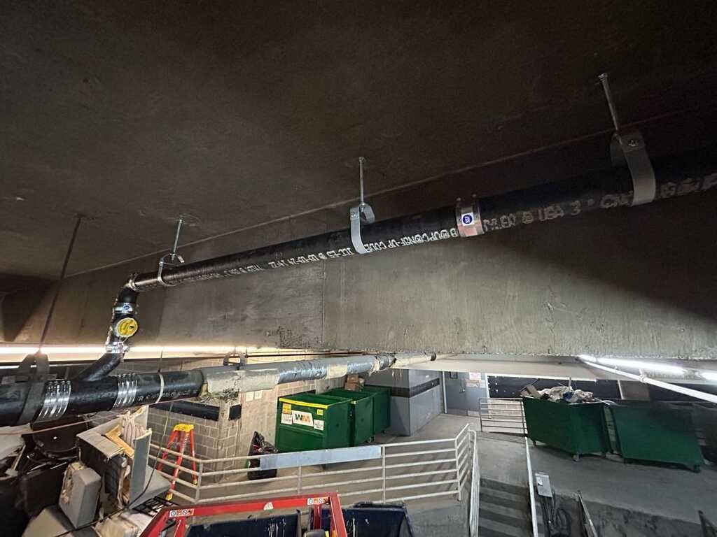 Large concrete tunnel ceiling with pipes, cables, and construction barriers at an underground site