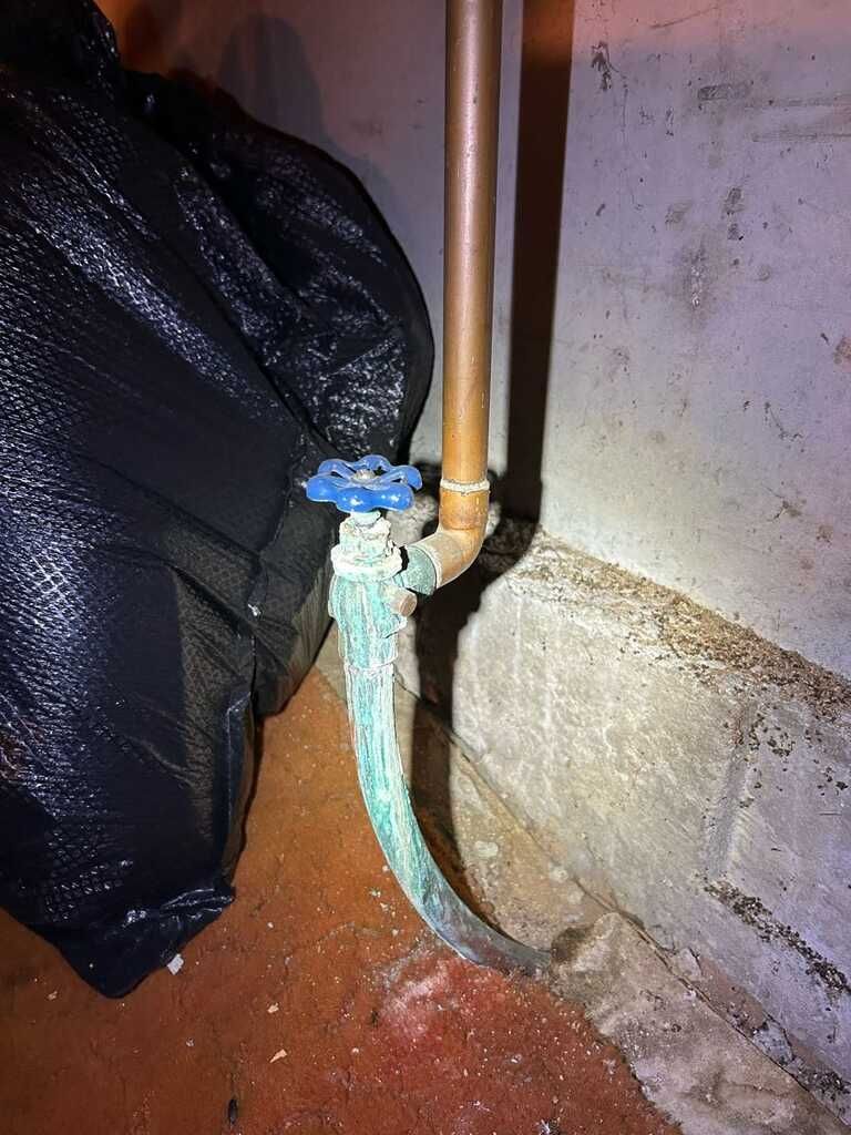 Leaking outdoor water hose connected to a brass pipe valve beside a wall, with wet ground below