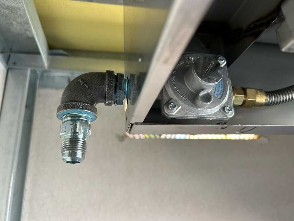 Close-up of a metal pipe fitting and valve assembly inside a machine or cabinet.