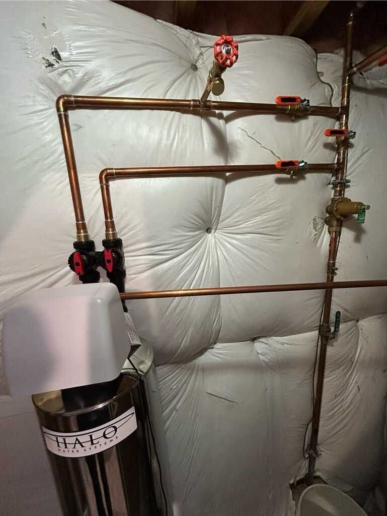 Copper pipes and valves mounted on a wall beside a water heater in a utility room