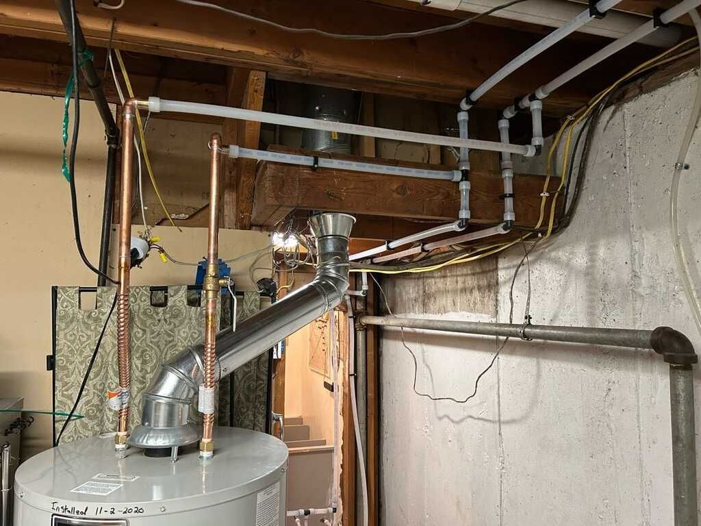 Hot water heater with metal venting and exposed pipes in a basement utility area.