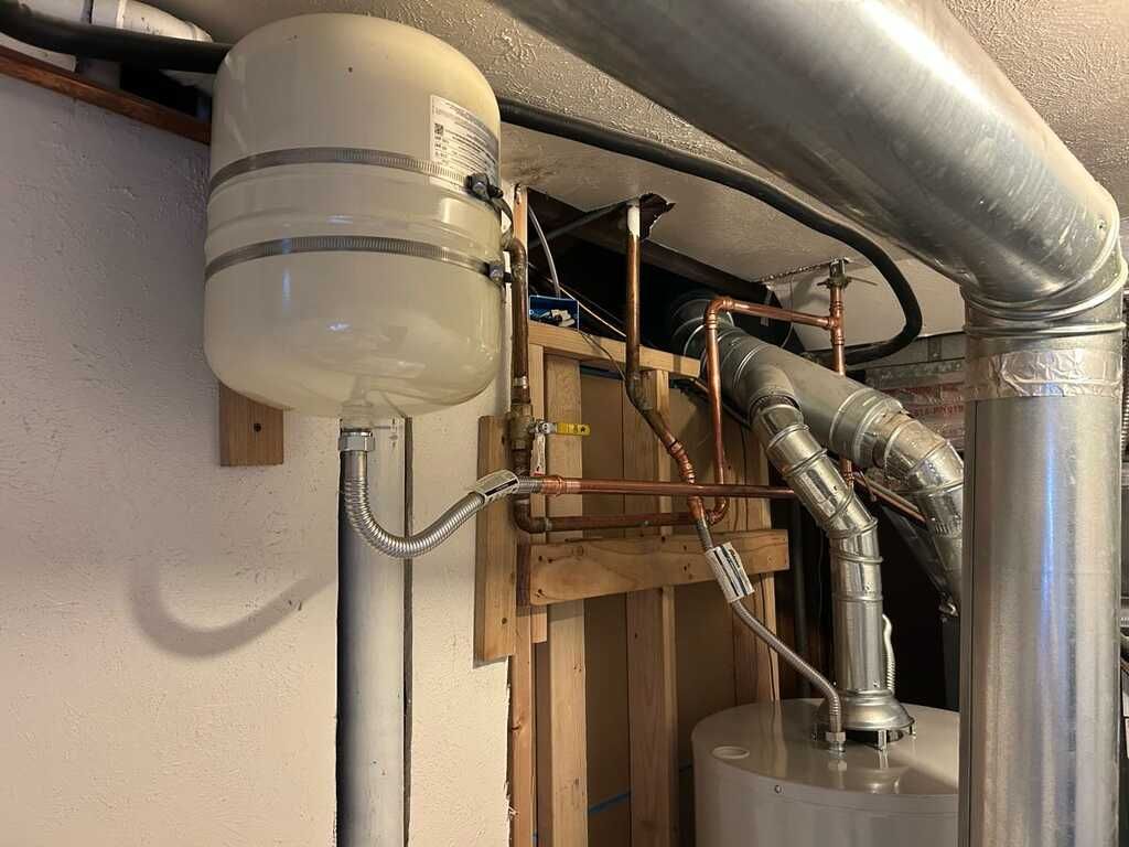 Basement mechanical area with water heater tank, exposed pipes, and ductwork near unfinished framing
