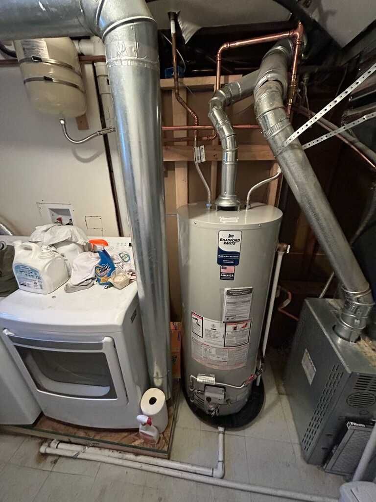 Utility closet with water heater, furnace, and exposed ductwork and piping.