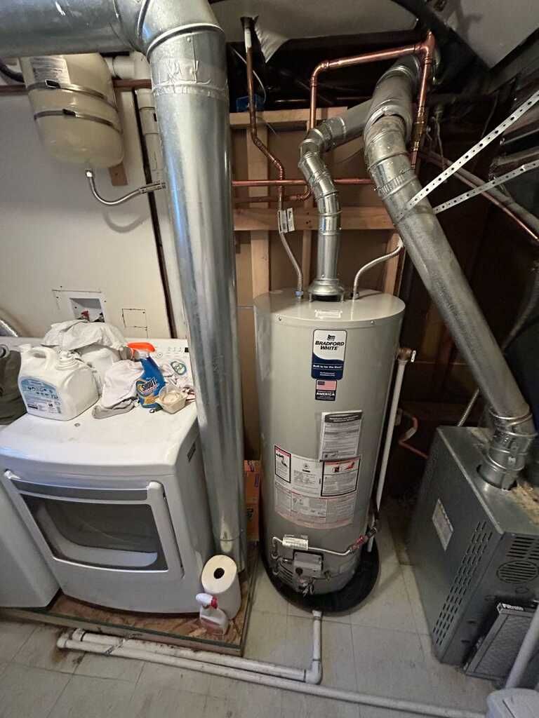 Utility closet with water heater, furnace, and exposed ductwork and piping.