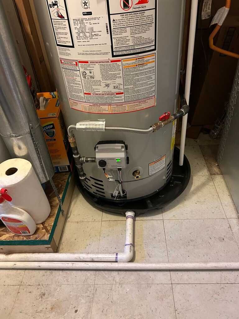 Water heater in a utility closet with exposed white PVC piping and a roll of paper towels on the left.