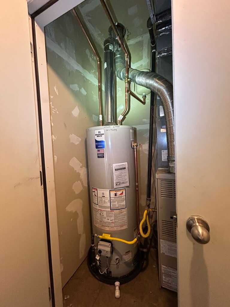 Water heater and furnace in a narrow utility closet with exposed pipes and ducts.