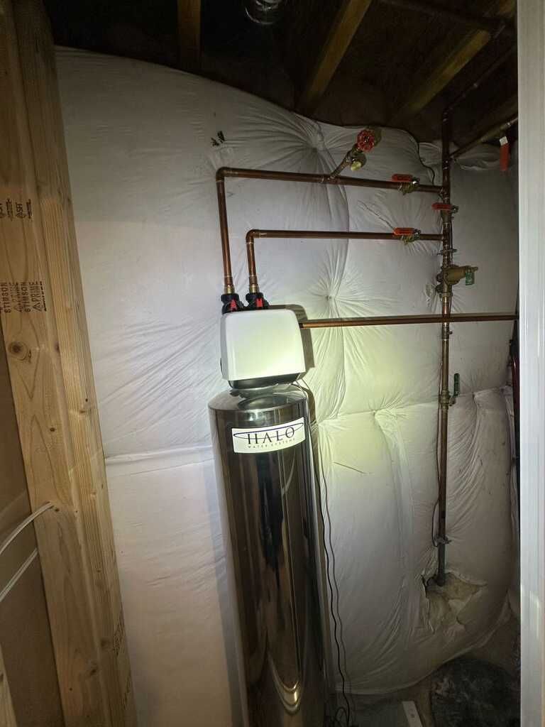 Basement water softener with copper pipes and insulated walls above a large tank