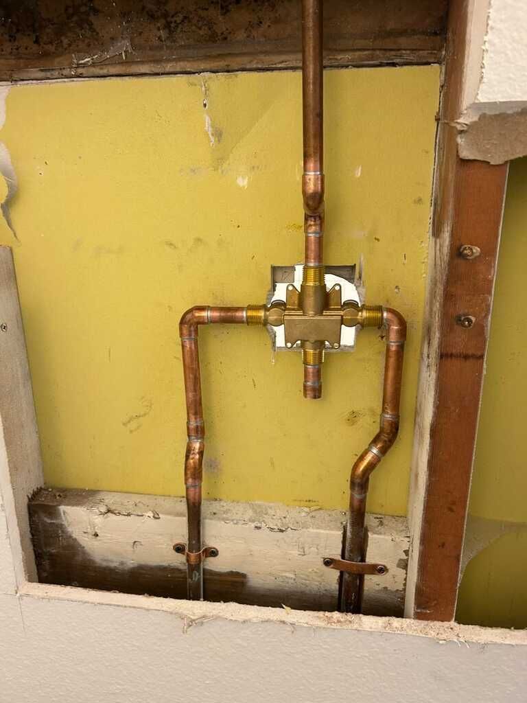 Exposed copper plumbing pipes and a brass valve in a wall cavity with yellow insulation backing.