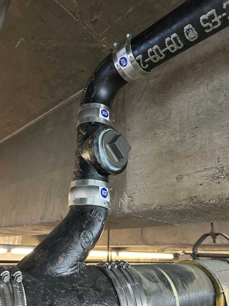 Close-up of black insulated pipes connected by metal couplings in a mechanical room.