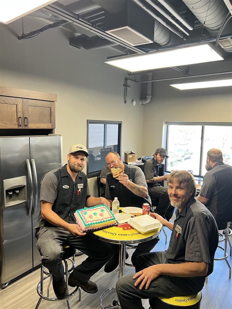 Men in work attire at a table, eating and celebrating with cake in a break room. | Joe's Auto and Tire