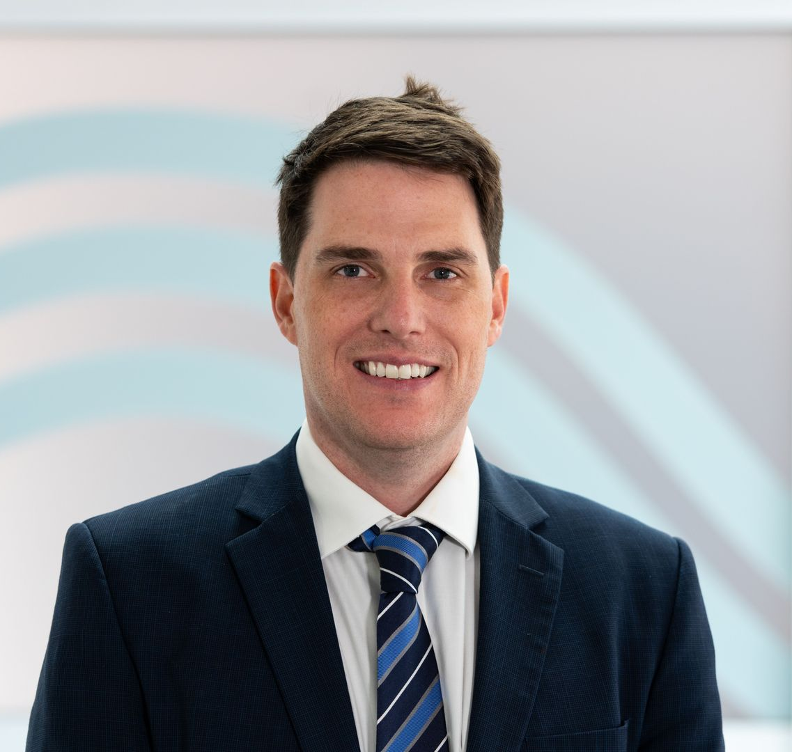 Dr Tom Moloney suit and tie is smiling for the camera .