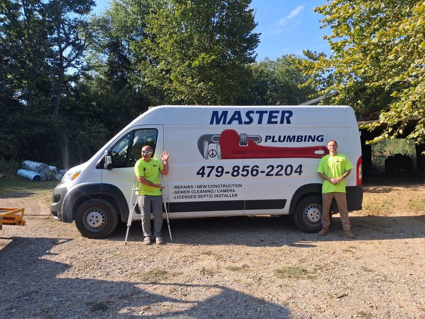 White Master Plumbing van parked on grass near trees, with logo and phone number visible.