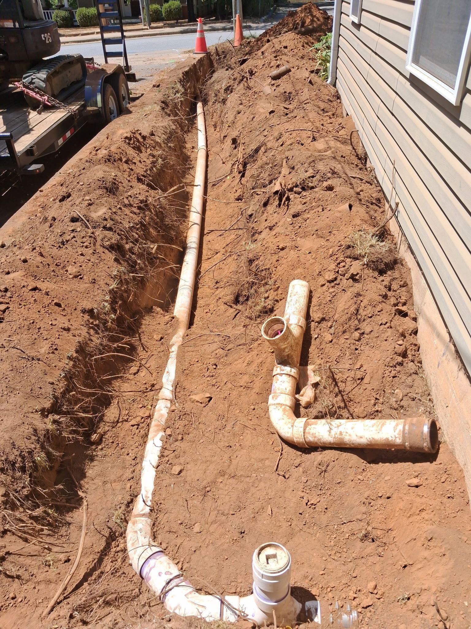 Construction workers installing a large pipe in a muddy trench with heavy machinery nearby