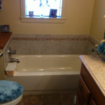 Bathroom with a cream bathtub, tan walls, granite counter, and blue stool by a small window.