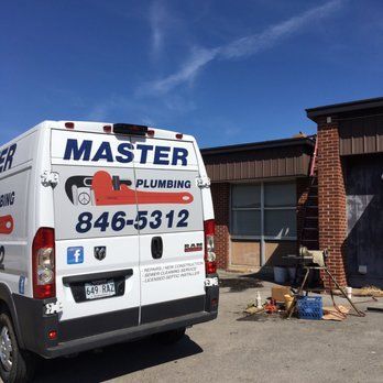 Master Plumbing van parked beside a brick building, with tools and a ladder near the entrance.