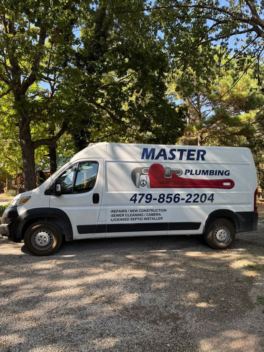 White Master Plumbing van parked on grass near trees, with logo and phone number visible.